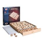 Scatola del Sudoku BOHS accanto alla tavoletta in legno con griglia 9x9, cassetto aperto con le tessere numerate e il libretto dei puzzle